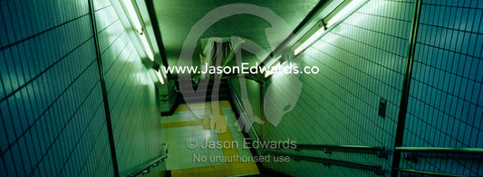 A stairwell illuminated by flourescent tubes descends to a subway. Ikebukuro Station, Tokyo, Japan.