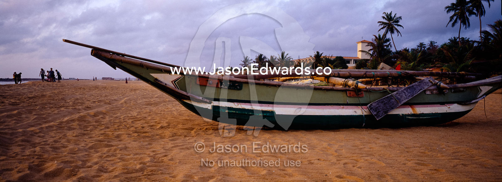 A small fishing boat rests on a tropical island beach at sunset. Negombo Beach, Sri Lanka.