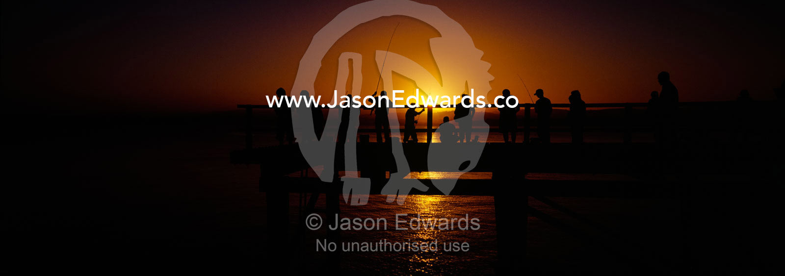 Holiday makers and fishermen in silhouette crowd a jetty at sunset. Merimbula, New South Wales, Australia.