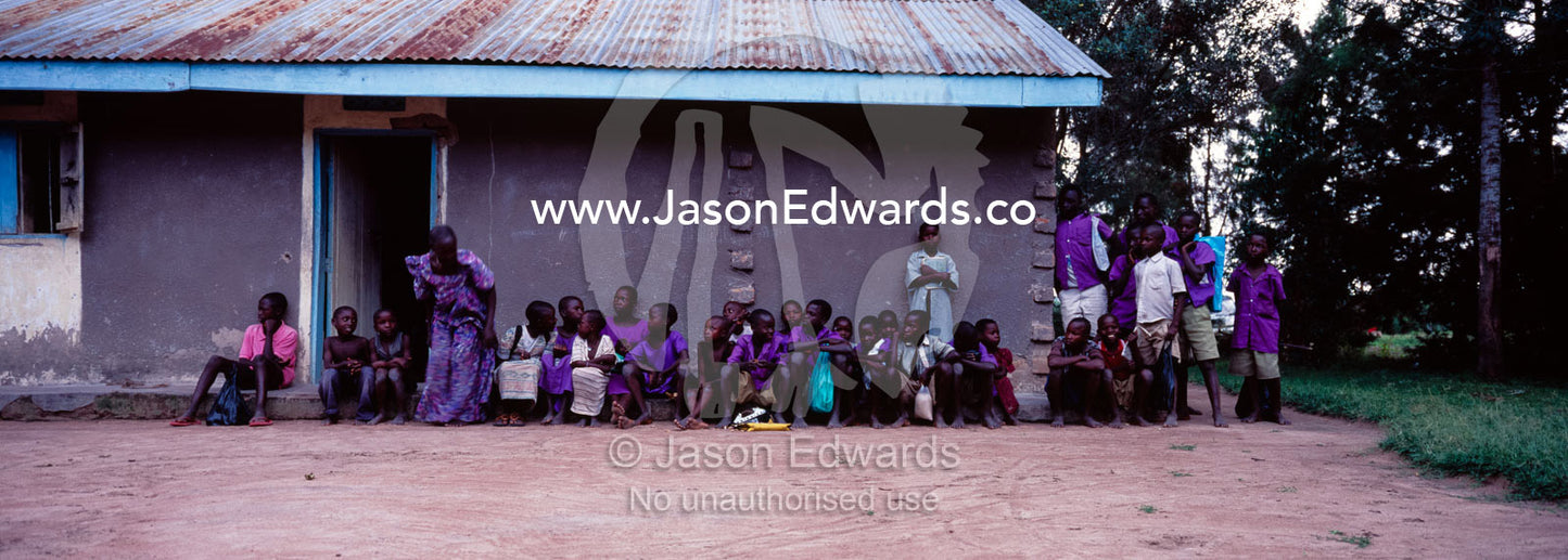 School children rest from the heat under the eave of a village home. Tororo District, Uganda.