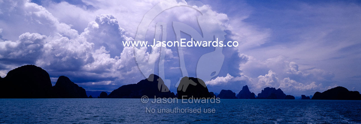 Tropical storm clouds billow over rugged volcanic islands lining the horizon. Phang Nga Bay Marine National Park, Phuket, Thailand.