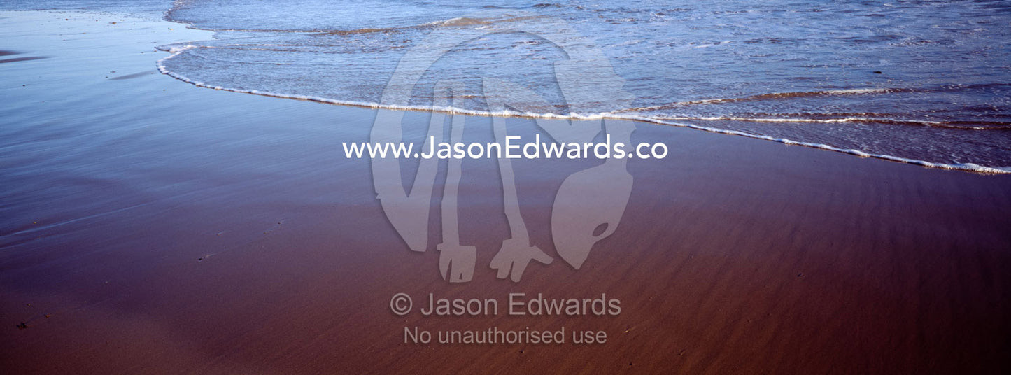 The leading edge of a wave creeps up onto the beach at low tide. Jan Juc, Victoria, Australia.