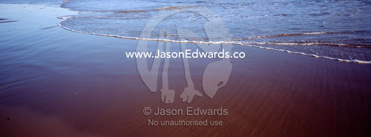 The leading edge of a wave creeps up onto the beach at low tide. Jan Juc, Victoria, Australia.