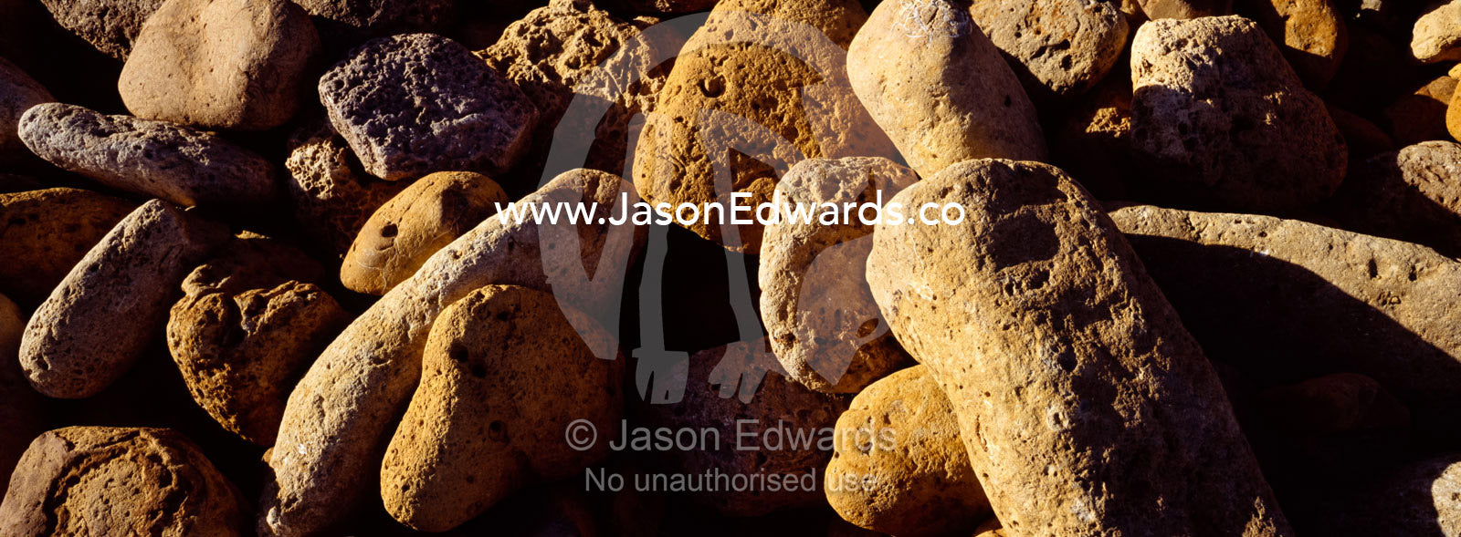 Sunset casts deep shadows over a tumble of boulders on a rocky beach. Jan Juc, Victoria, Australia.