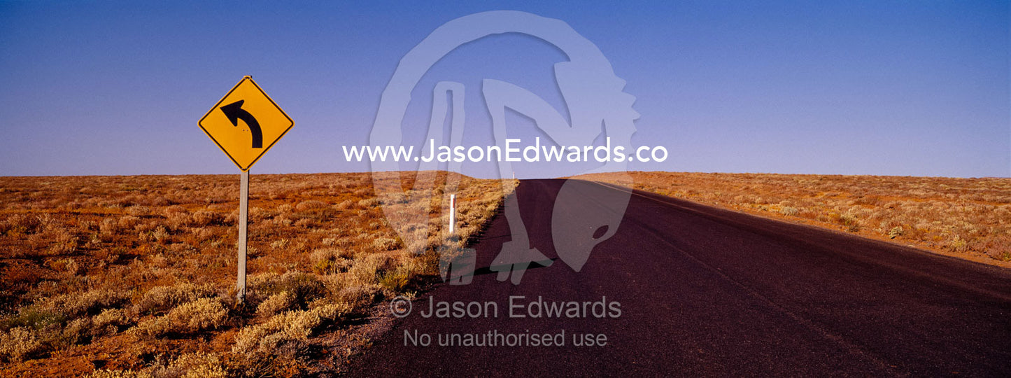 A sign warns of a rare bend in the road on a featureless desert plain. near Broken Hill, New South Wales, Australia.