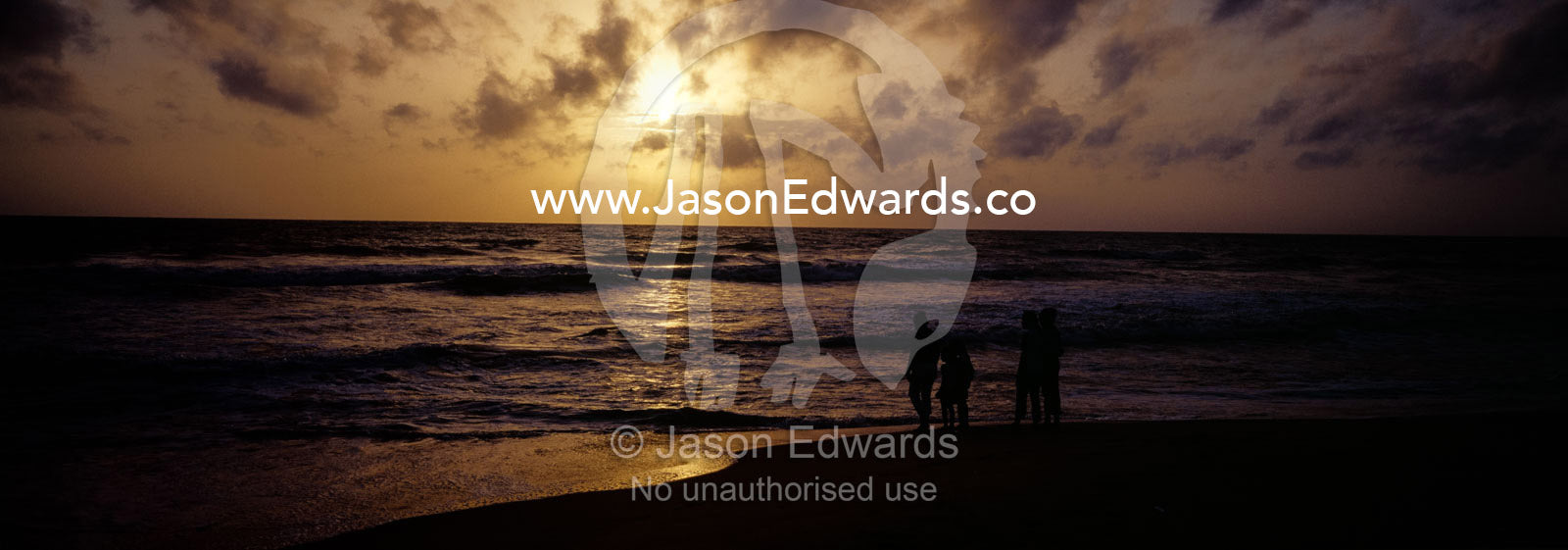 People wade in shallow waves on a tropical island beach at sunset. Negombo Beach, Sri Lanka.