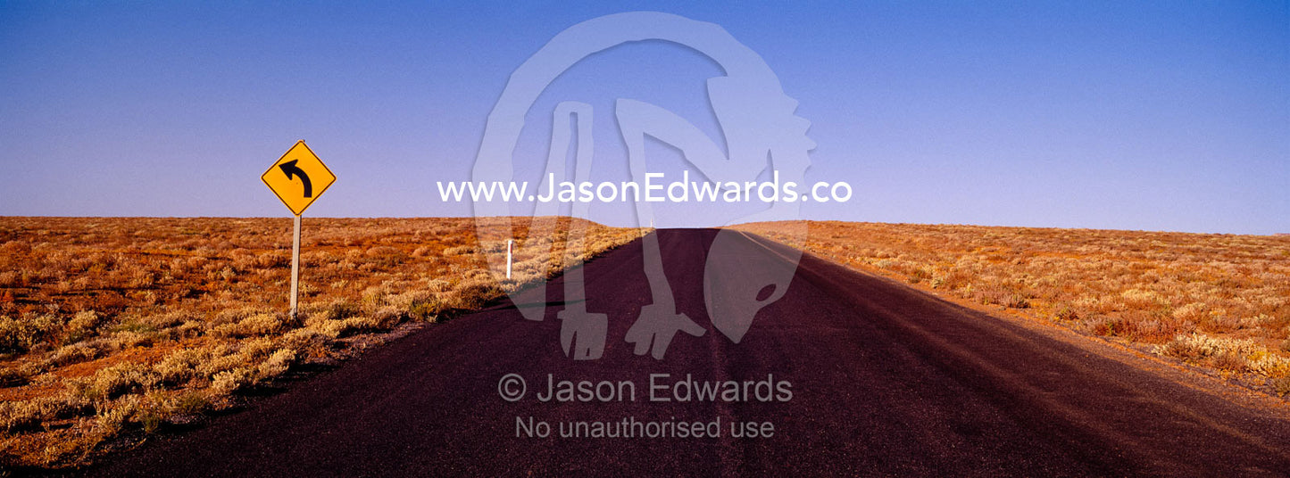 A sign warns of a rare bend in the road on a featureless desert plain. near Broken Hill, New South Wales, Australia.