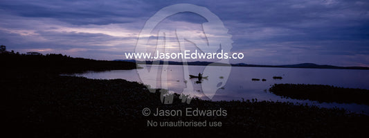 A fisherman in a dugout canoe casts a pole on Lake Victoria at dawn. Lake Victoria, Kampala, Uganda.