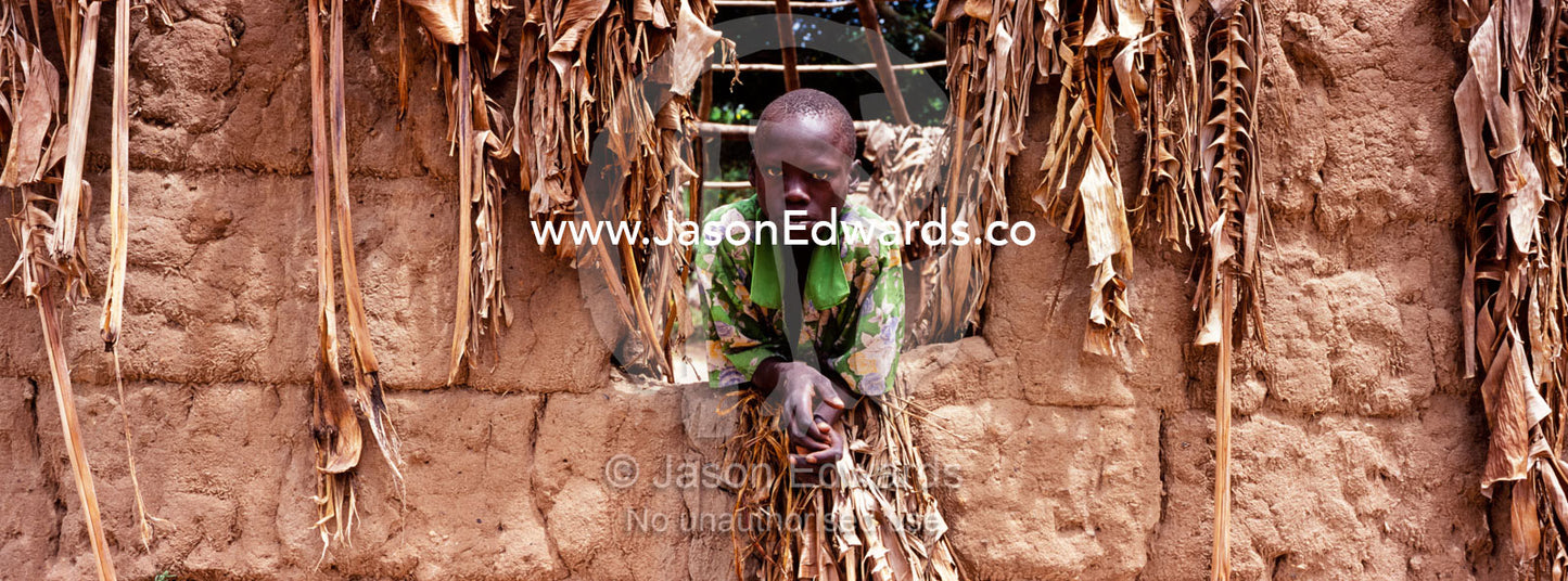 The intense stare of a boy resting from the heat in a mud hut window. Tororo District, Uganda.