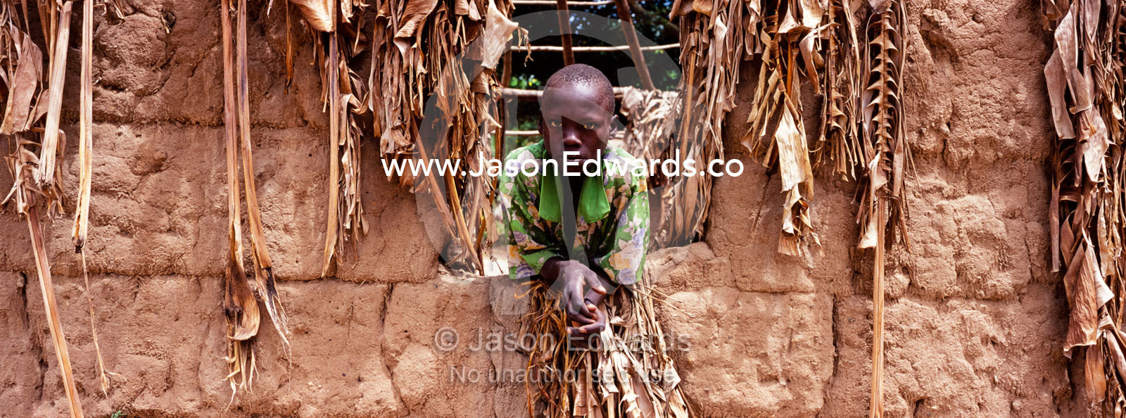 The intense stare of a boy resting from the heat in a mud hut window. Tororo District, Uganda.