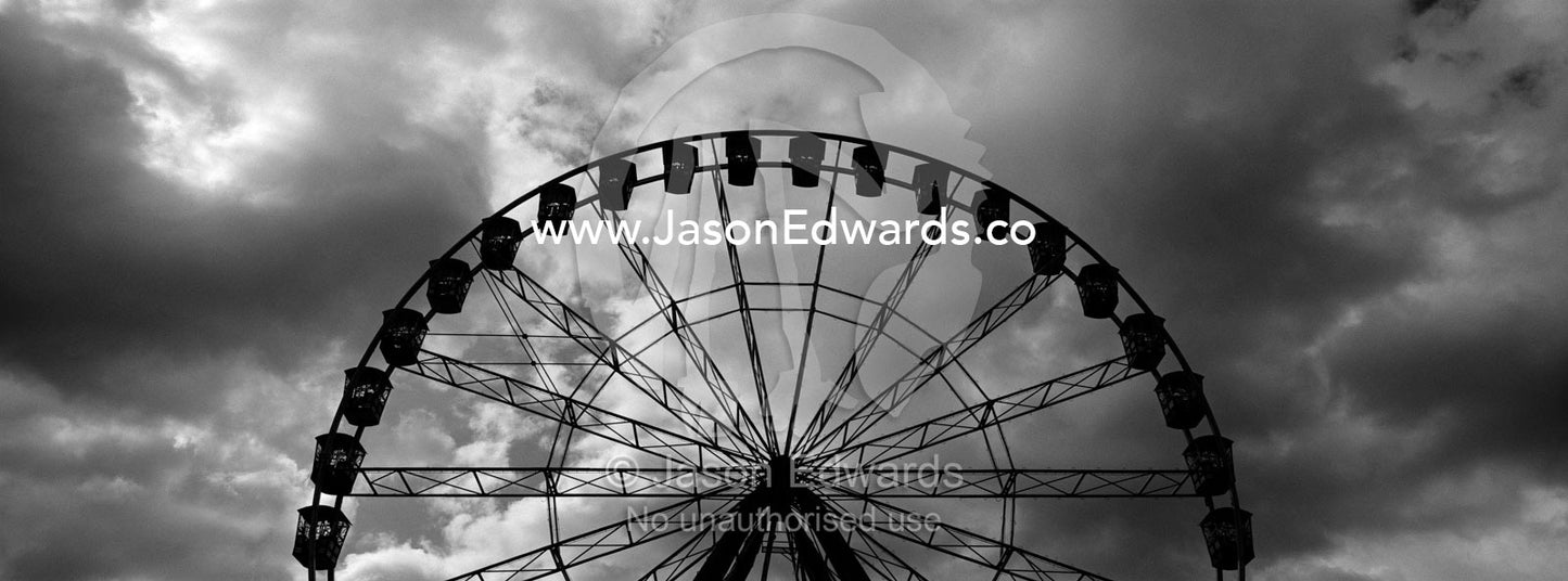 A silhouette of an immense ferris wheel rises into a stormy grey sky. Melbourne, Victoria, Australia.