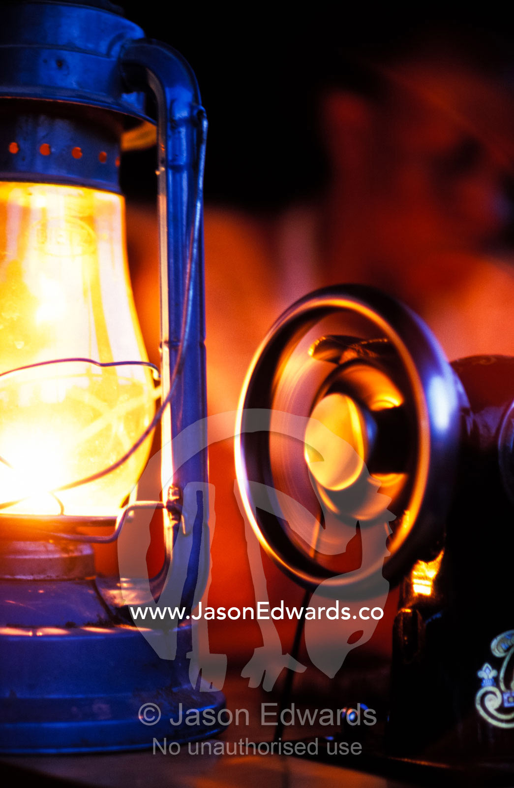 An antique sewing machine spinning for a seamstress by lantern light. Tororo District, Uganda.