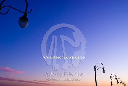 Antique lights hang over the boardwalk of Santa Monica pier at sunset. Santa Monica, Los Angeles, California, United States of America.