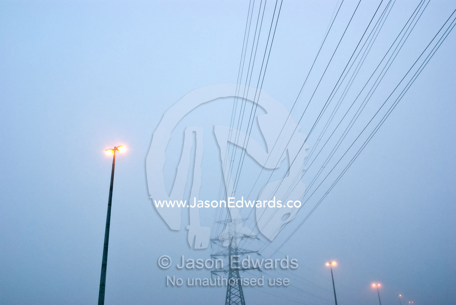 Electricity tower, power cables and freeway lights on a foggy morning. Point Cook, Victoria, Australia.