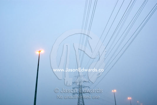 Electricity tower, power cables and freeway lights on a foggy morning. Point Cook, Victoria, Australia.