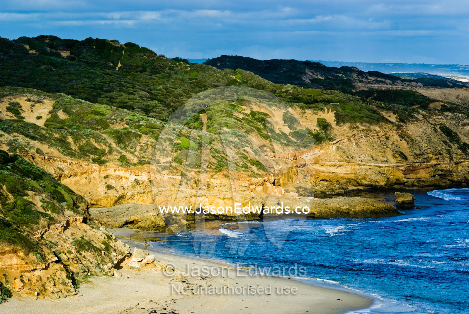 Dappled sunlight falls across rugged sandstone cliffs over the ocean. Mornington National Park, Victoria, Australia.