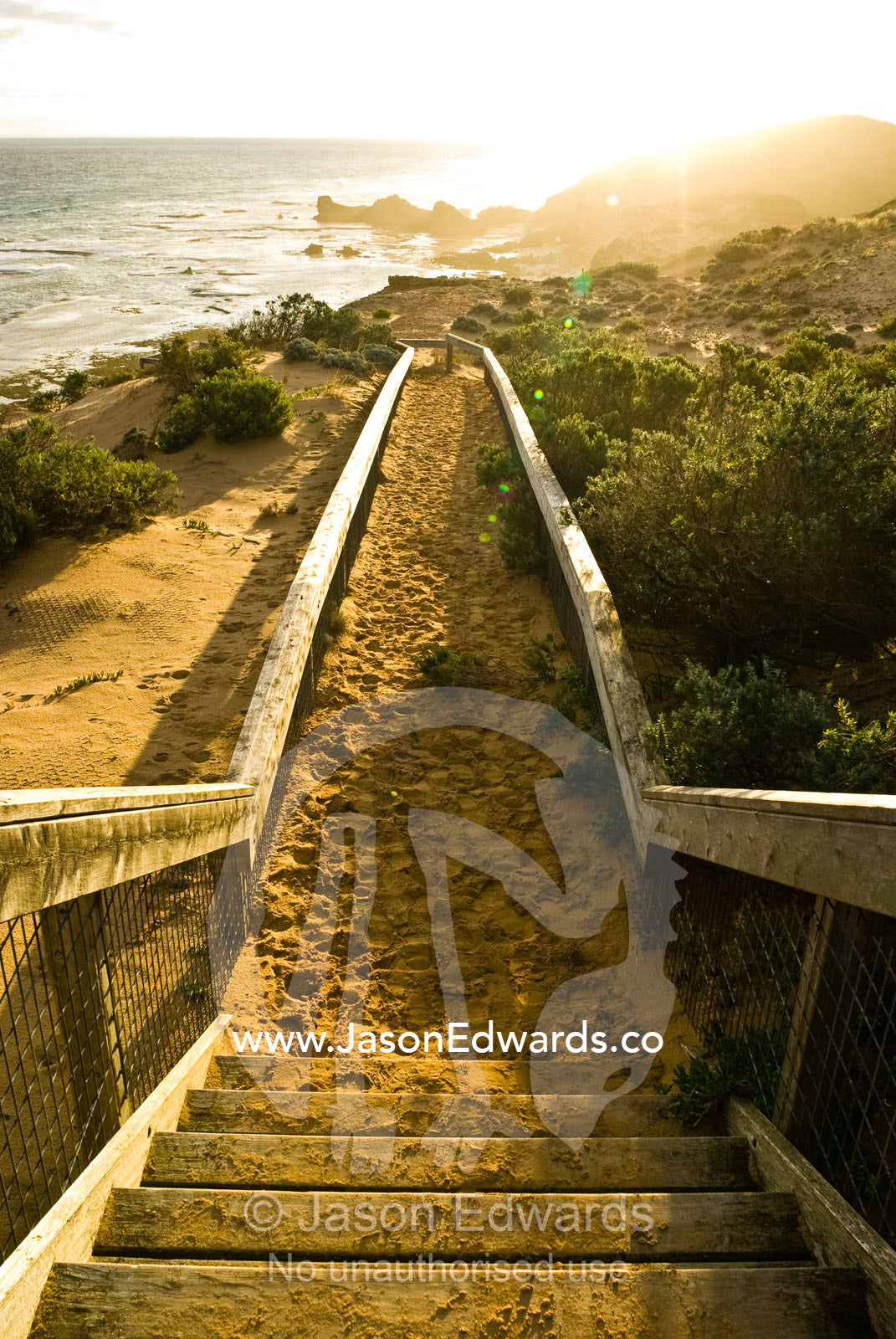 A stairwell leads down to a rugged and remote sandy beach at sunset. Mornington National Park, Victoria, Australia.