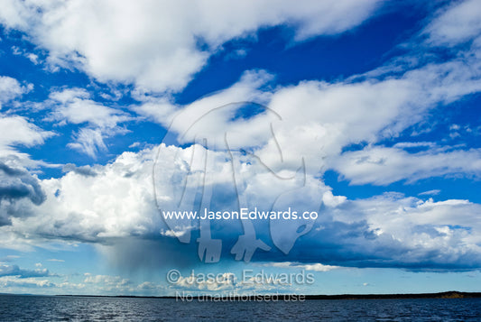 A rain storm pours down from a billowing thunderhead over a vast lake. The Lakes National Park, East Gippsland, Victoria, Australia.