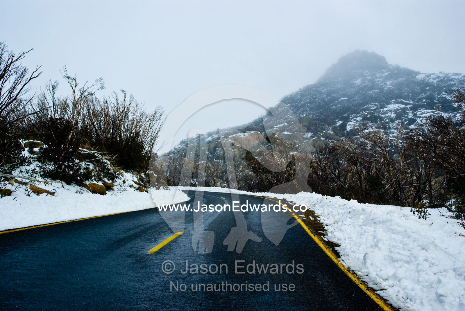 An icy road winds through a rugged alpine pass shrouded in snow. Mount Buffalo National Park, Victoria, Australia.