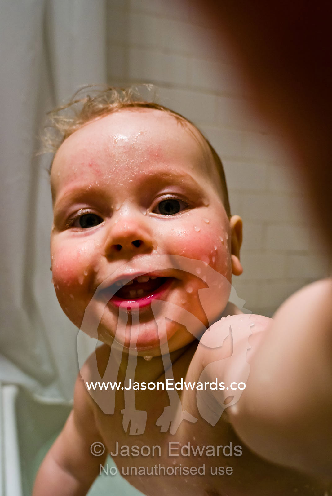 A ten month old infant plays with the camera whilst having a bath. North Carlton, Victoria, Australia.