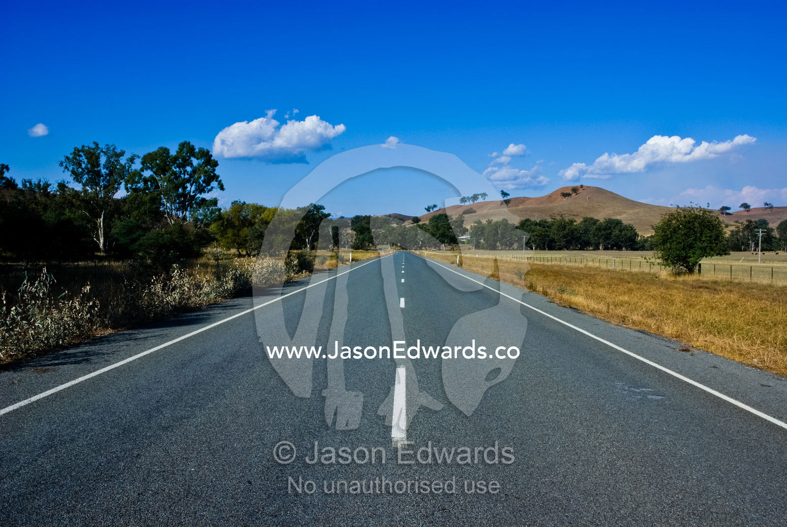 An empty country road passes through farmland and rolling hills. near Yea, Victoria, Australia.