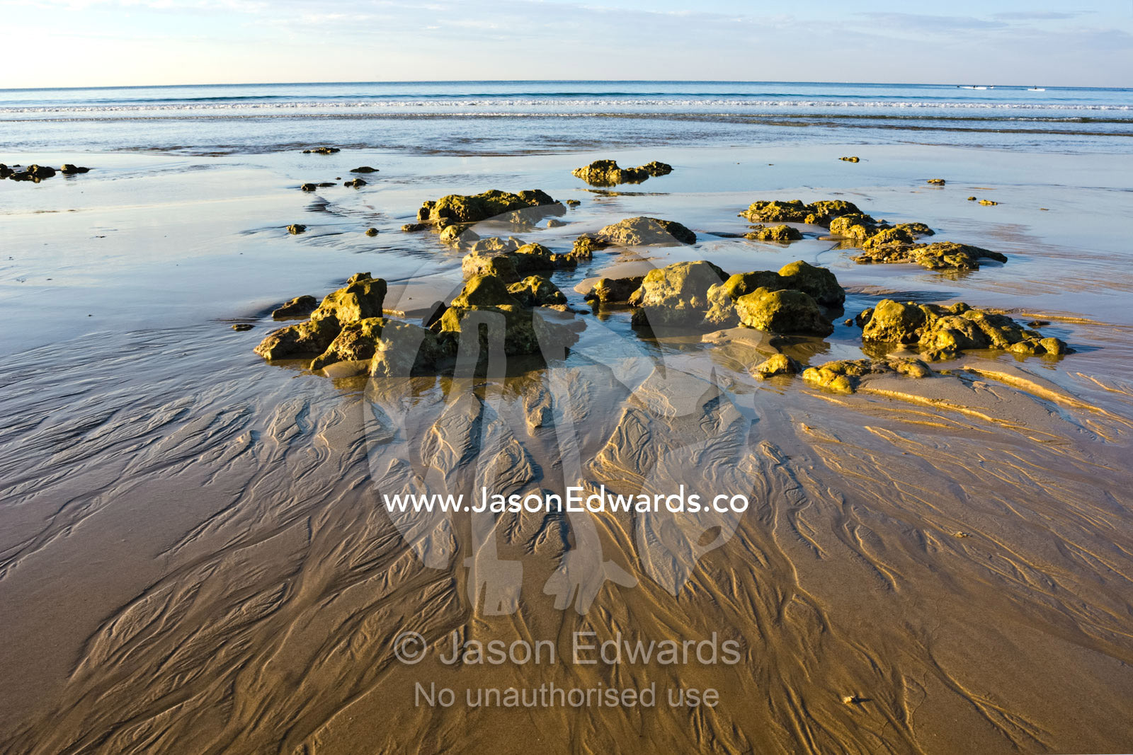 The receding tide leaves patterns in the sand around small boulders. Point Danger, Torquay, Victoria, Australia.