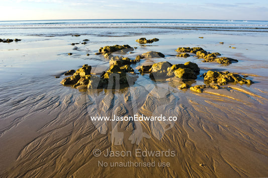 The receding tide leaves patterns in the sand around small boulders. Point Danger, Torquay, Victoria, Australia.