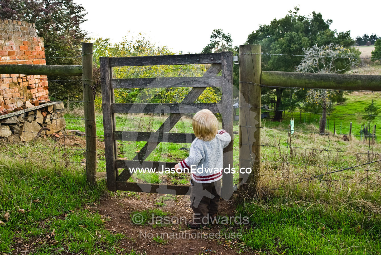 A toddler prepares to embark on an adventure through a farm gate. Woodhall, Tasmania, Australia.