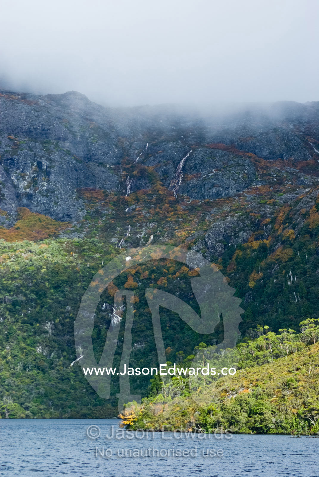 Alpine waterfalls cascade down rugged, storm shrouded granite peaks. Cradle Mountain Lake St Clair National Park, Tasmania, Australia.