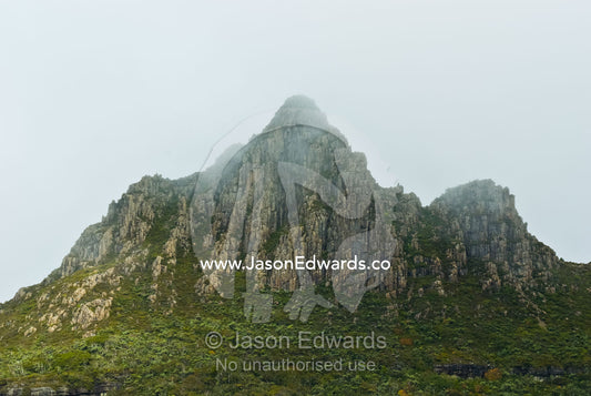 Clouds and mist shroud the jagged granite peaks of Cradle Mountain. Cradle Mountain Lake St Clair National Park, Tasmania, Australia.