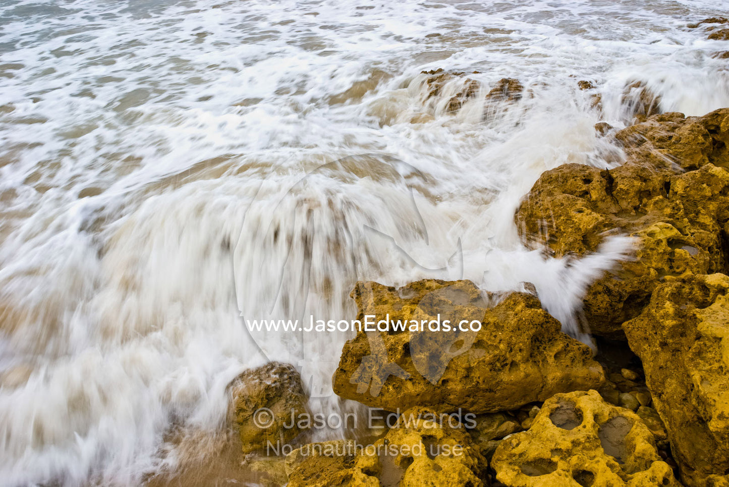 Waves crash over sandstone boulders on a rocky shoreline. Point Impossible, Victoria, Australia.