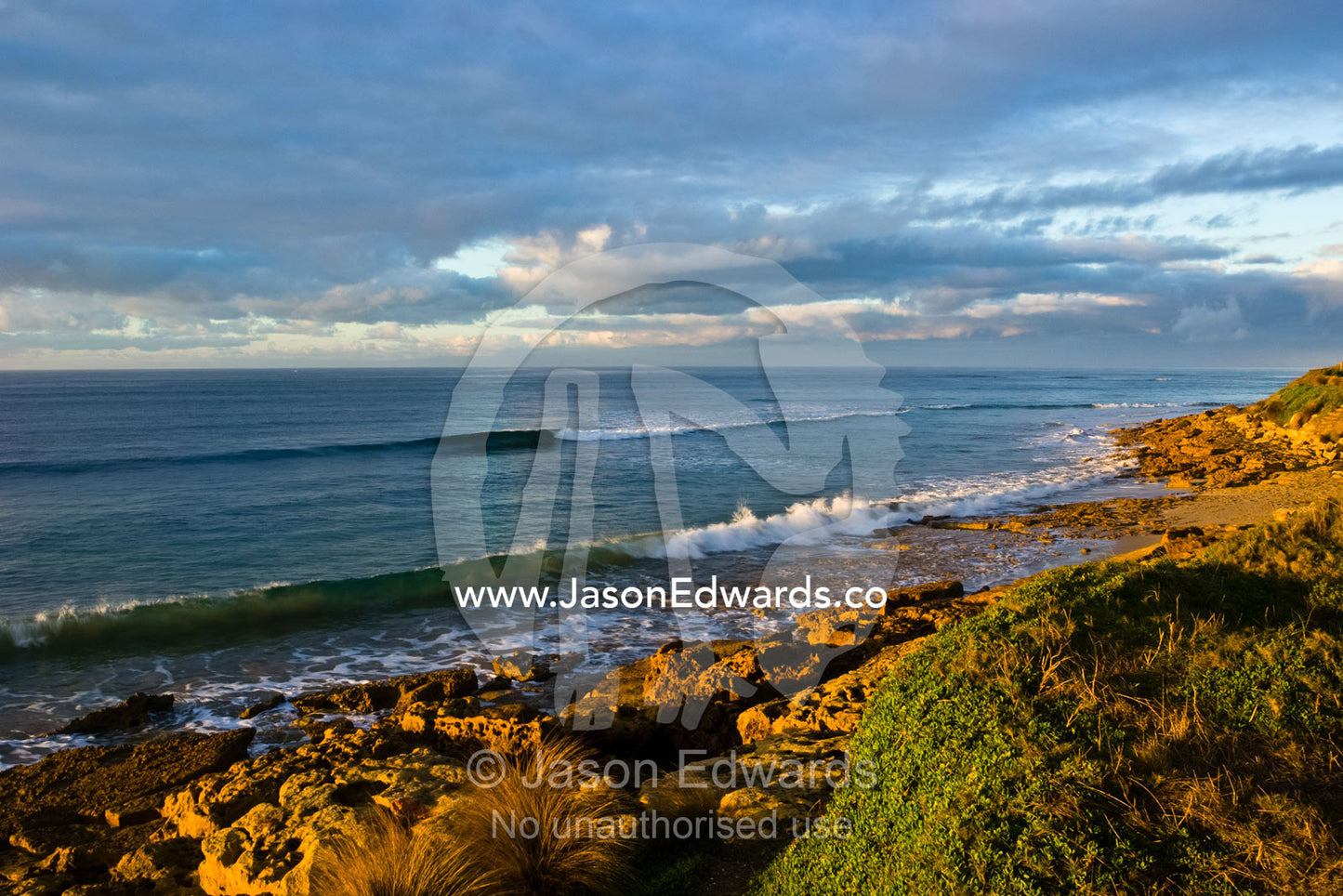 Small, tranquil waves roll onto a remote and rocky coastline at dawn. Point Impossible, Victoria, Australia.