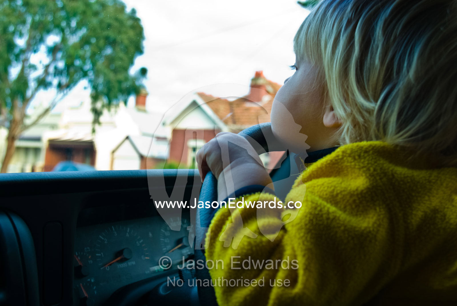 A toddler peers over the steering wheel of an SUV pretending to drive. North Carlton, Victoria, Australia.