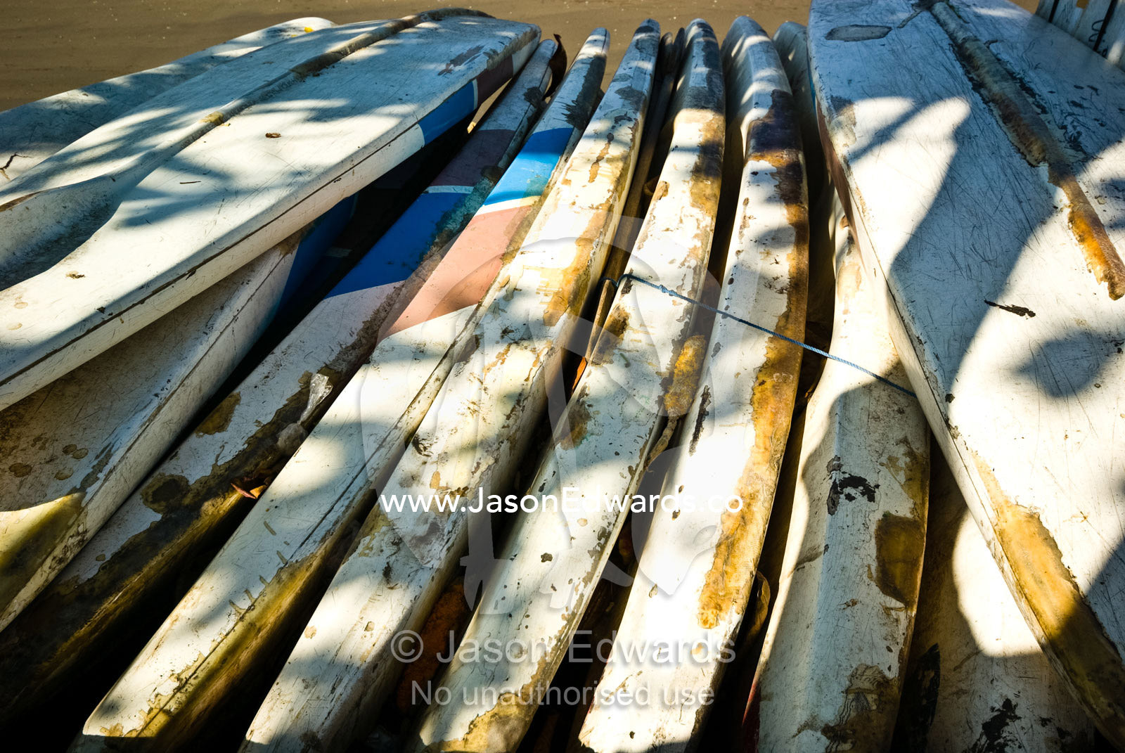 Weathered and beaten surfboards for tourist hire rest on the beach. Sanur, Bali, Indonesia.