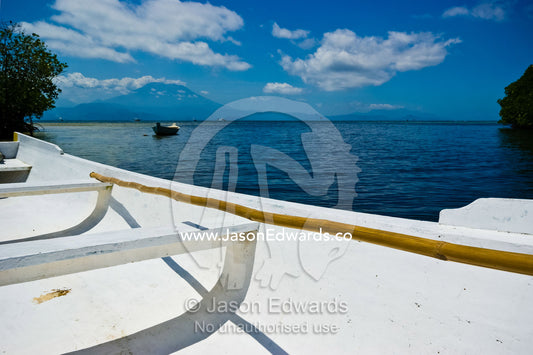 A cane pole rests in an elegant long boat in a bay near a volcano. Nusa Lembongan Island, Bali, Indonesia