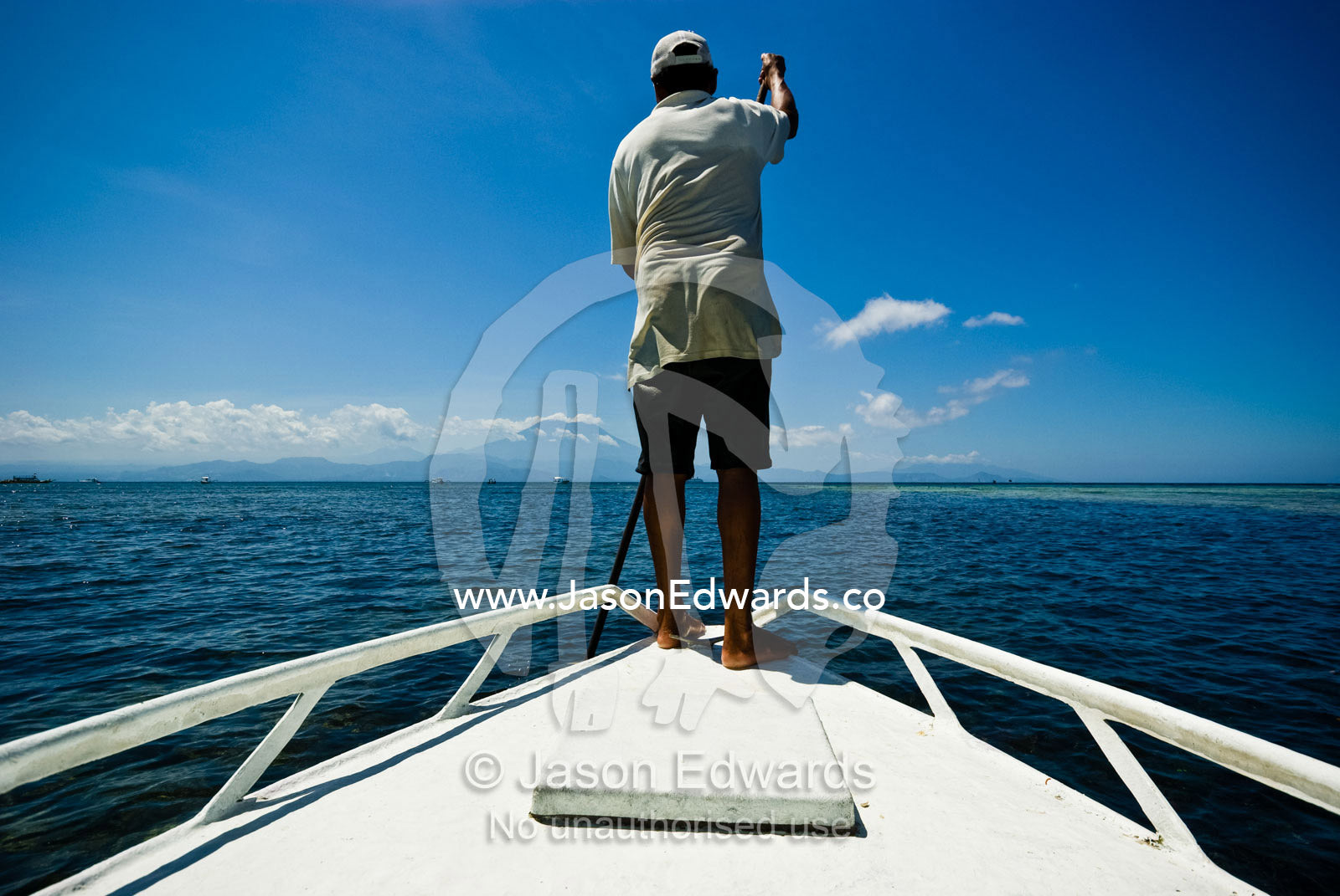 A captain guides his long boat between jagged reefs using a cane pole Nusa Lembongan Island, Bali, Indonesia.