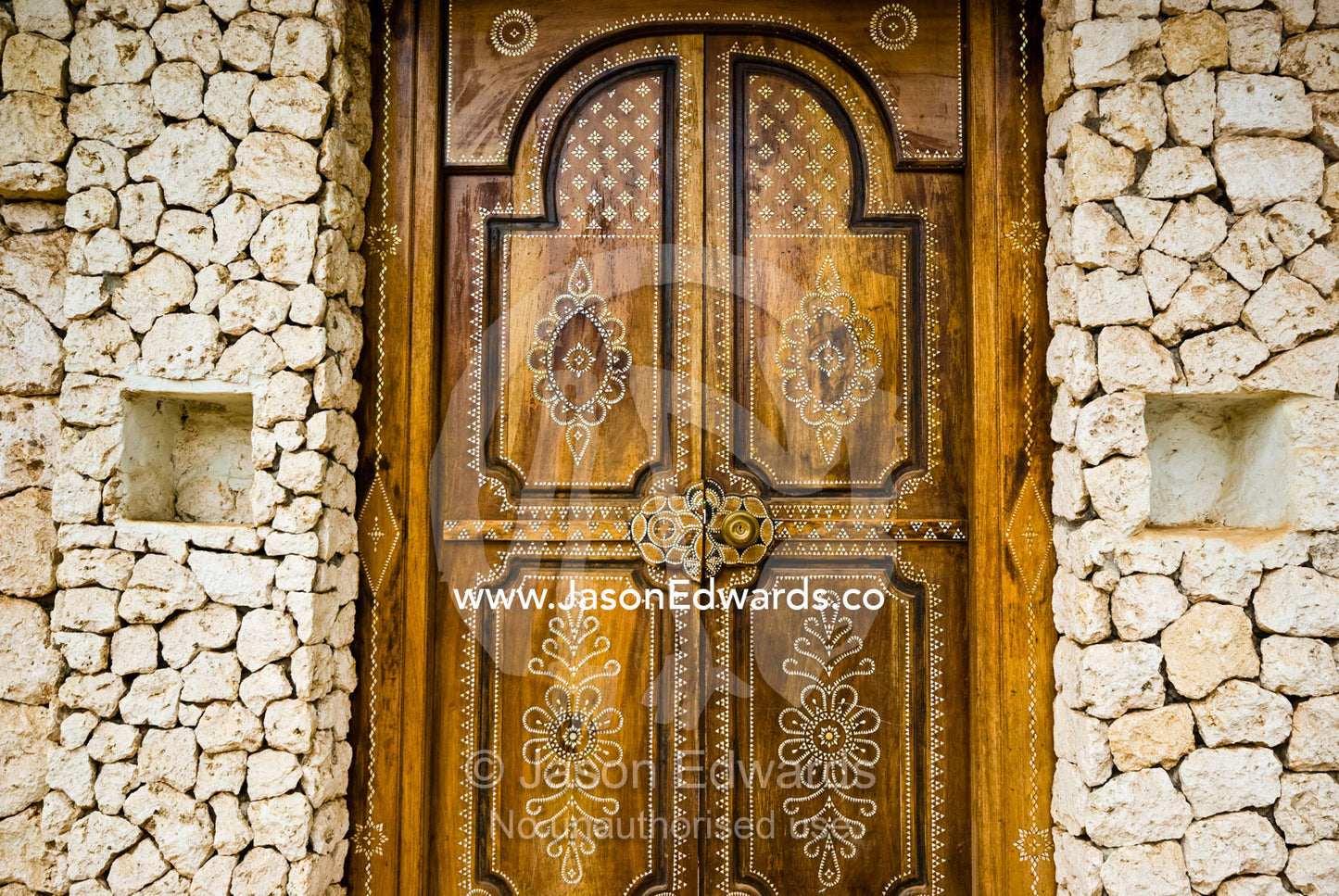 Artistic Petra Dura design on a timber door set in a stone wall. Bukit Peninsula, Bali, Indonesia.