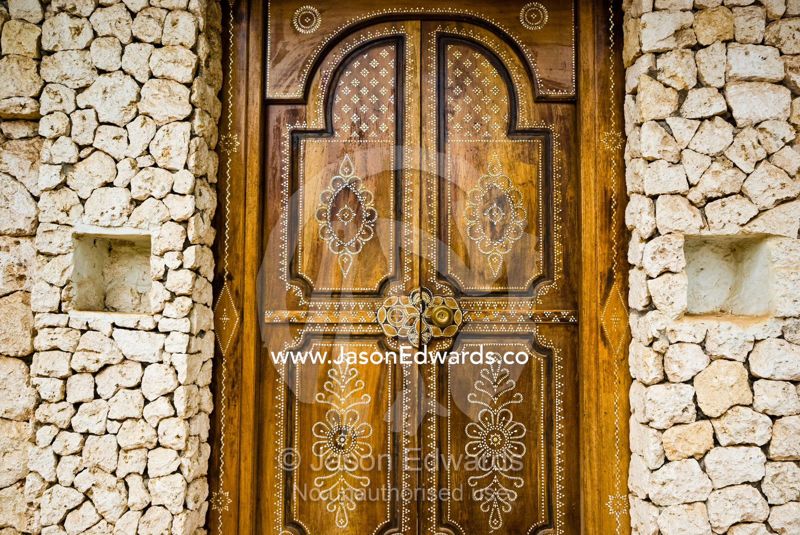 Artistic Petra Dura design on a timber door set in a stone wall. Bukit Peninsula, Bali, Indonesia.
