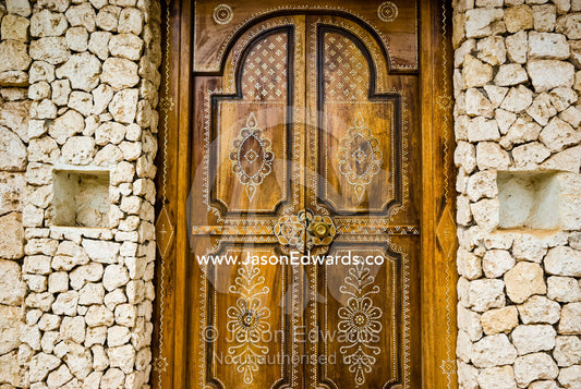 Artistic Petra Dura design on a timber door set in a stone wall. Bukit Peninsula, Bali, Indonesia.