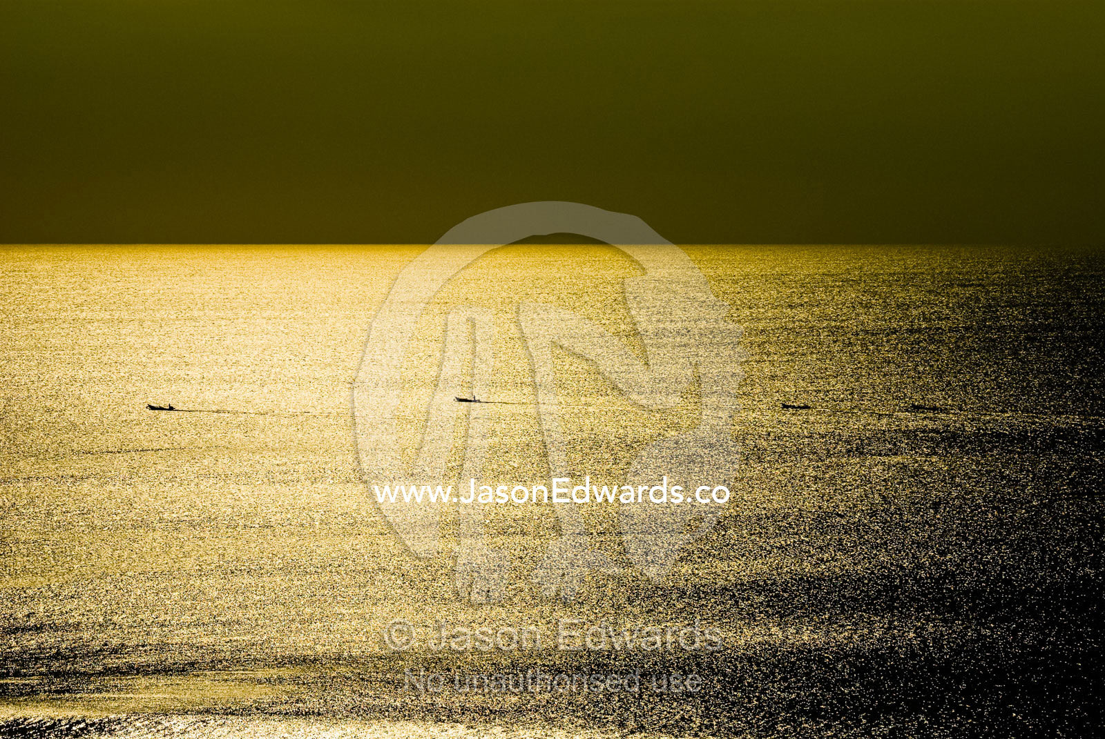 The silhouettes of tiny fishing boats heading out to sea at sunset. Bali Strait, Bukit Peninsula, Bali, Indonesia.
