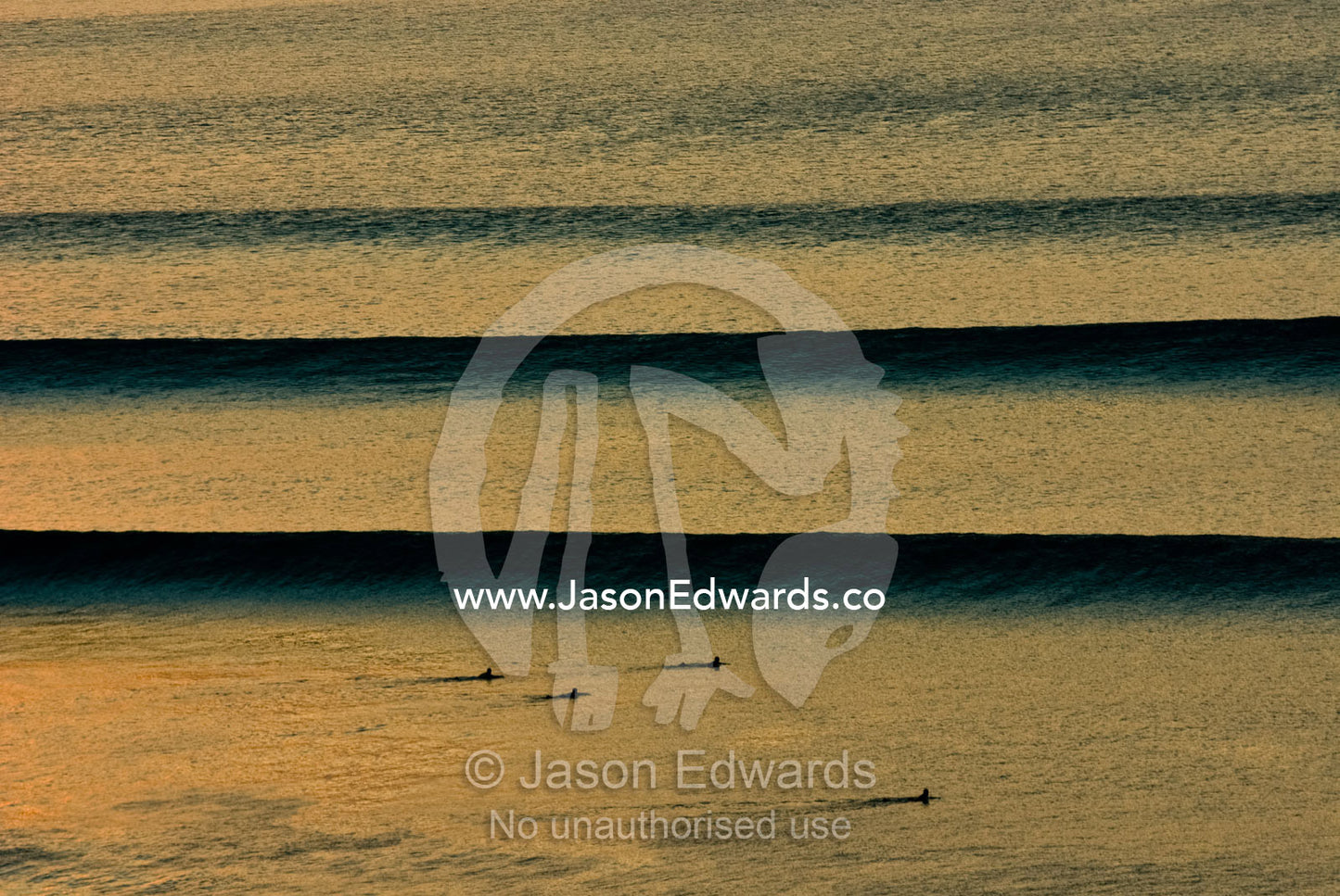 Surfers await beautiful clean sunset waves as they roll in over a reef Impossibles, Bukit Peninsula, Bali, Indonesia.