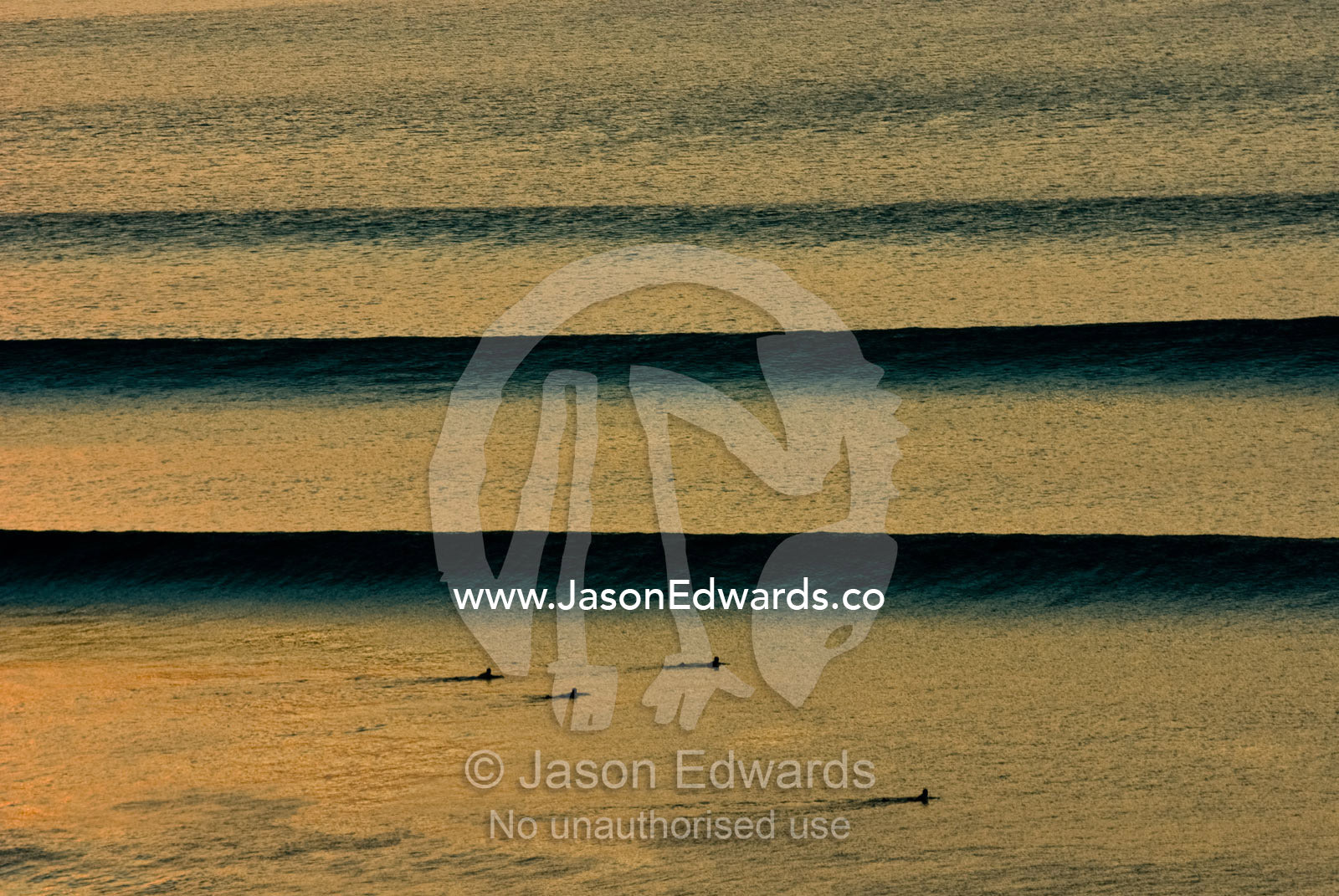 Surfers await beautiful clean sunset waves as they roll in over a reef Impossibles, Bukit Peninsula, Bali, Indonesia.