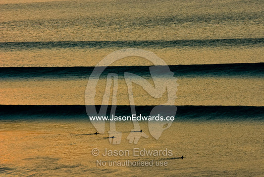 Surfers await beautiful clean sunset waves as they roll in over a reef Impossibles, Bukit Peninsula, Bali, Indonesia.