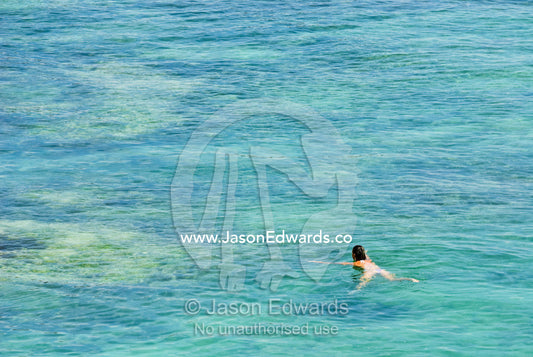 A lady enjoys swimming over the reef at Uluwatu's famed surfing break. Uluwatu, Bukit Peninsula, Bali, Indonesia.
