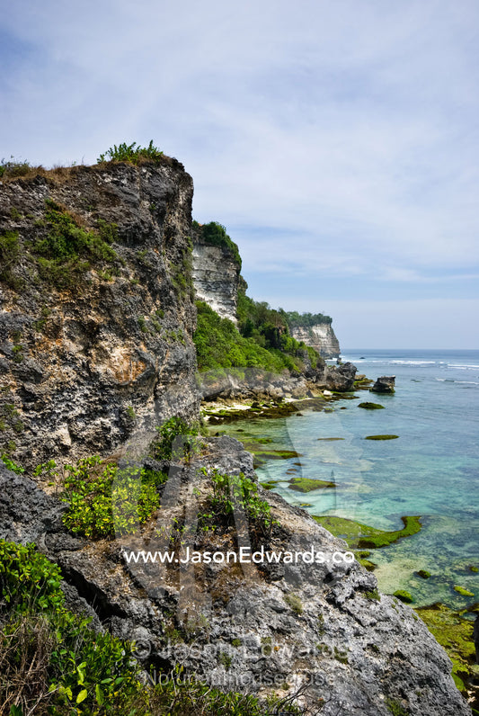 Rugged limestone cliffs overlook tranquil tropical bays and reefs. Uluwatu, Bukit Peninsula, Bali, Indonesia.