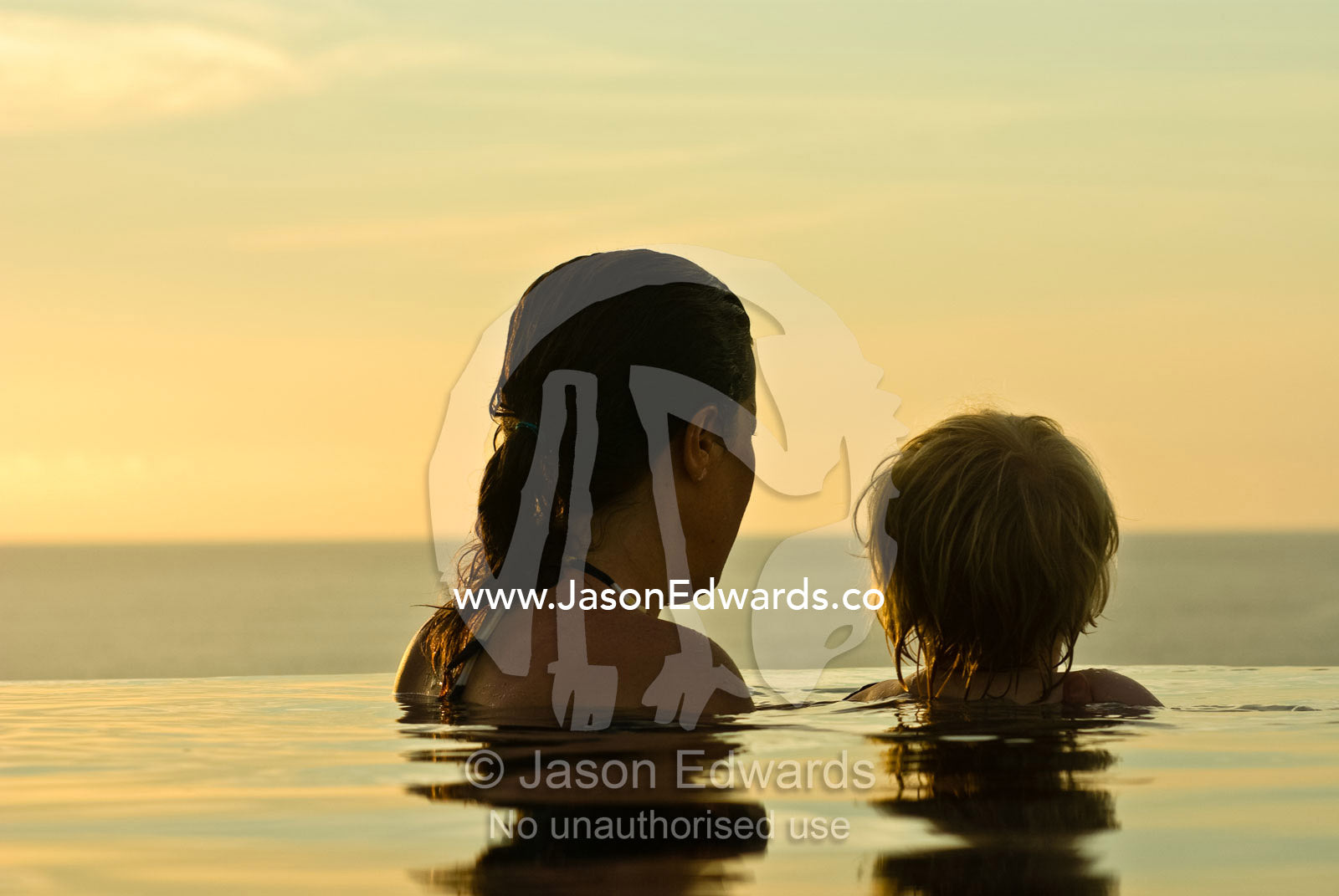 A mother and son watch the sunset from a horizon pool in a villa. The Temple Lodge, Bukit Peninsula, Bali, Indonesia.