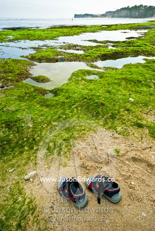 A toddlers sandals rest in the sand on an empty beach at low tide. Bingin, Bukit Peninsula, Bali, Indonesia.