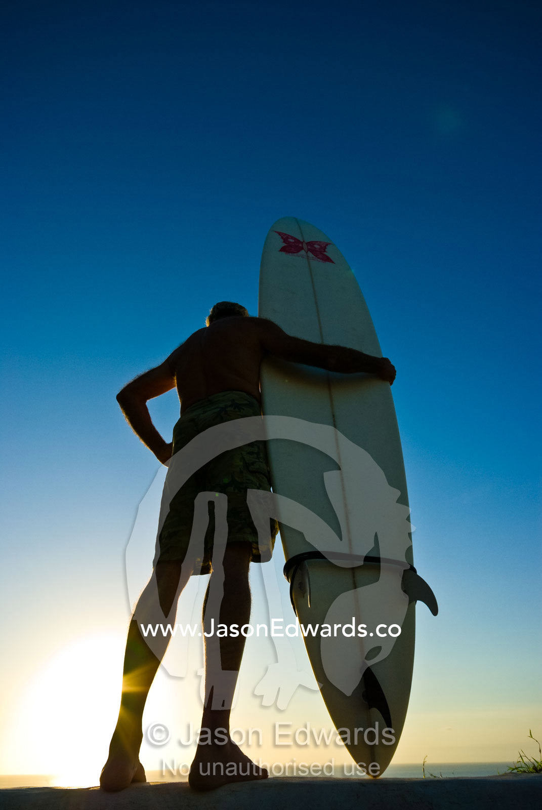 A mature surfer watches the waves from a cliff top at sunset. Bukit Peninsula, Bali, Indonesia.