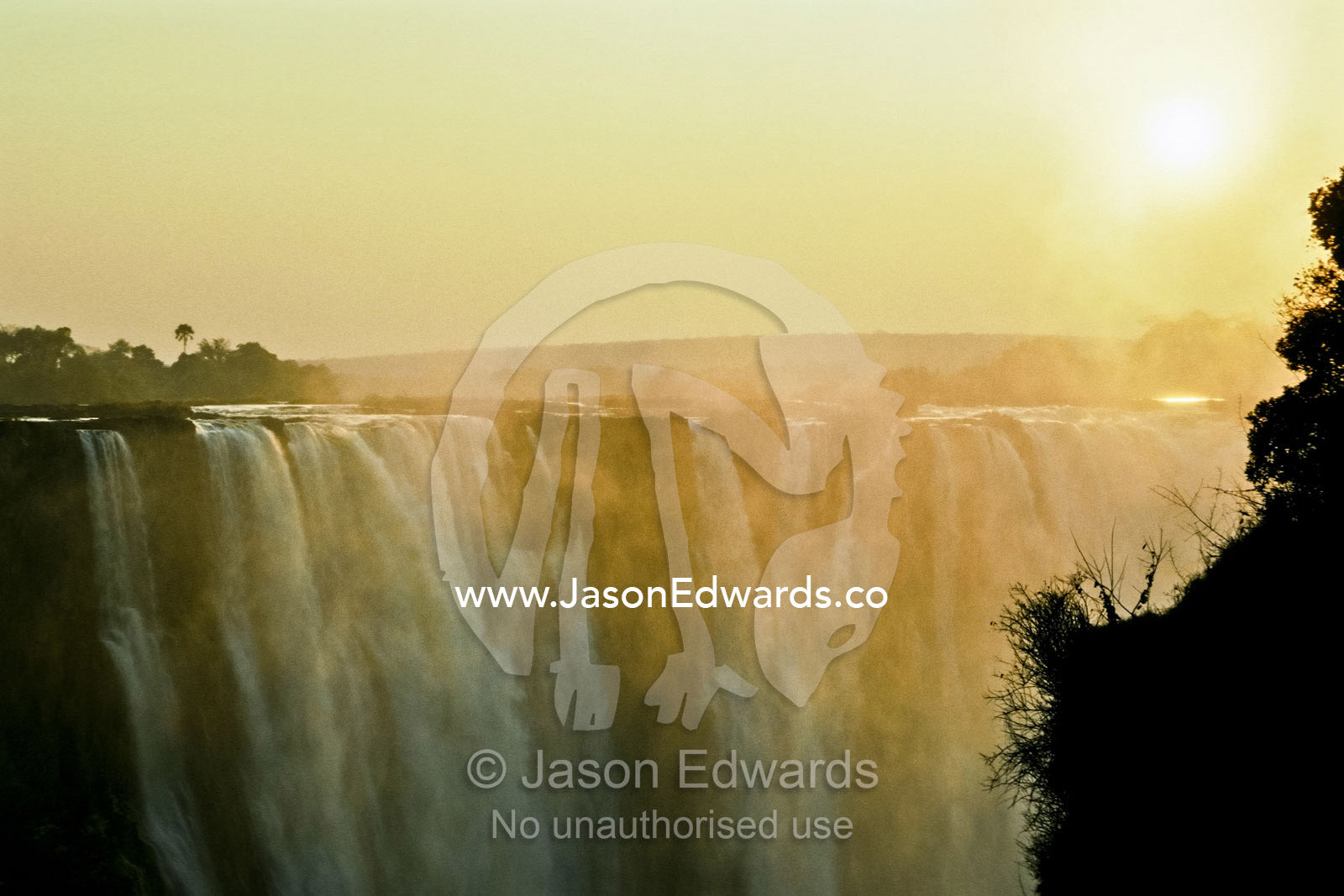 A golden dawn cuts through the mist and spray over Victoria Falls. Victoria Falls National Park, Zimbabwe.