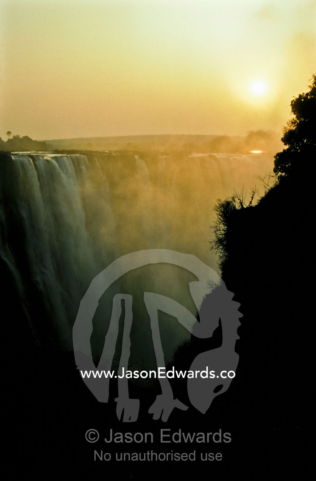 A golden dawn cuts through the mist and spray over Victoria Falls. Victoria Falls National Park, Zimbabwe.